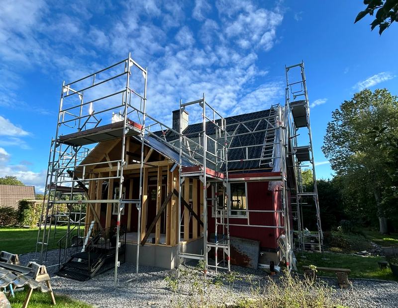 Byggnadsställning med gaveltorn och trapptorn runt ett rött trähus